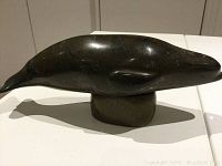 Side view of dark green-gray soapstone whale carving mounted on stand