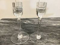Full view of pair of clear crystal candlesticks on a marble surface.