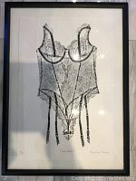 Full front view of framed black-and-white lace bodysuit print leaning against a light tile floor, reflections visible on glass