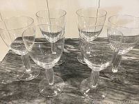 Six clear glass goblets arranged in two rows on a marble surface, showing the set in its entirety.