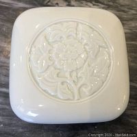Top view of white square porcelain box lid with embossed circular floral motif.