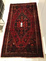 Full view of red and navy geometric patterned rug on light floor with water bottle for scale