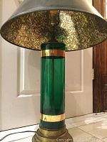 Close-up of the green glass lamp base with gold bands and brass base, showing the cylindrical shape and material details.