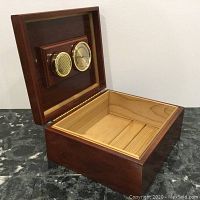 Open wooden cigar humidor box showing light wood interior and mounted hygrometer and humidifier on lid.