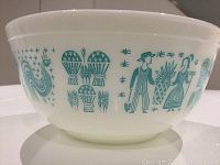 Side view of the vintage Pyrex bowl showing blue farmer, wheat sheaf, and rooster graphics on white milk glass.