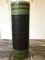 Front view of the tall cylindrical vase showing the green and brown striped glaze with a rough textured dark center.