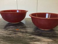 Side view of two red Pyrex C bowls on grey marble surface with a penny for size comparison.