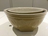 Two ceramic mixing bowls nested, showing beige exterior with embossed geometric designs and smooth interior glaze.
