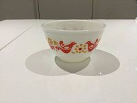 Side view of vintage white glass Pyrex mixing bowl featuring orange and yellow bird and flower promotional pattern.
