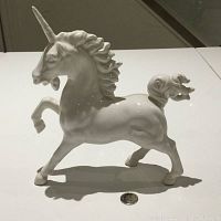 Porcelain unicorn figurine showing profile view with raised front leg and detailed mane and tail, glossy white porcelain finish.