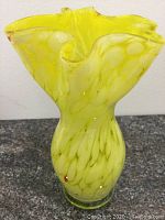 Front angle view of yellow Venetian glass vase showing wavy top edge and mottled pattern.