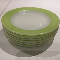 Stack of 8 lime green rimmed Pyrex plates stacked on top of each other showing edges and glossy surface.