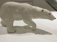 Side view of a glossy white ceramic polar bear figurine in walking posture on a flat surface.