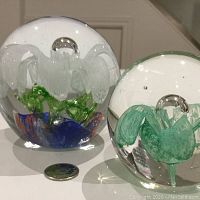Pair of mid-century Murano glass paperweights showing white and green three-dimensional flowers inside clear glass spheres with coin for scale.