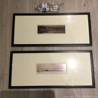Top and bottom rectangular framed pictures laid flat. Each features a small, centered landscape print with double white and beige mats and black frame. Includes water bottle for scale.