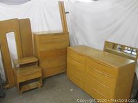 Wide shot of two bed panels (headboard, footboard) leaning, tall chest, low dresser, nightstand