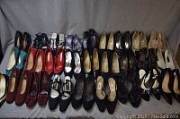Photo showing full collection of 27 pairs of women's heeled shoes in various colors and brands, arranged in rows on grey fabric background.