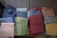 Image showing 12 assorted frilled linen table covers in multiple colors including blue, pink, green, red, orange, gray, and yellow, arranged on a beige couch.