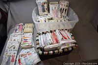 View showing two large containers filled with numerous folded paper sewing patterns for women's clothing, including identifiable brands such as Butterick and Burda.
