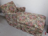 Side view of the chaise lounge showing floral tapestry upholstery, armrest, and skirted base.