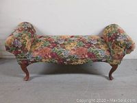 Full frontal view of rectangular end of bed seat covered in floral tapestry fabric with two rolled armrests and cherry stained curved legs.