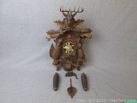 Front view of the full cuckoo clock with weights and pendulum laid out in front.