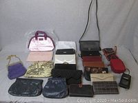 Overview of all ladies wallets and clutch handbags arranged on a flat surface showing different colors, materials and sizes including the tapestry style beaded bag and purple clutch with chain strap.