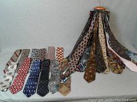 Overview of multiple men's silk ties arranged hanging and laid out on table, showing various patterns and colors.