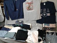 Lot display showing folded assorted men's XL t-shirts in various colors and designs including patriotic themes alongside a folded American flag.