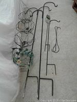 Photo showing collection of garden hooks and hanging baskets including wire baskets, two tall black double hanger hooks, smaller hooks, and metal stake with green glass cat face