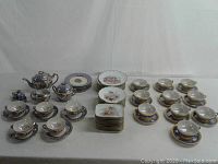 Full overview of the Noritake tea set, Limoges dishes, and Japanese iridescent cups and saucers arranged on a table, showing the variety and quantity of pieces