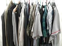 Clothing on hangers showing variety of dress pants, long sleeve shirts, two blazers, and a long wool coat