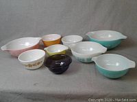Full view of all nine vintage Pyrex mixing bowls in various colors and patterns arranged on grey cloth.