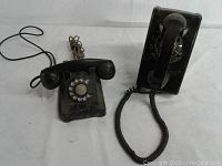 Overview of both vintage black rotary dial telephones, showing table and wall models, cords, and handsets