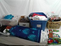 Multiple containers filled with folded fabric remnants and a large bolt of blue fabric with turquoise design laid out on a table