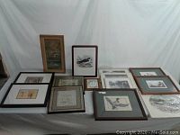 Photo showing 14 assorted framed wall hangings laid flat including embroidery, photographs, prints and artwork.