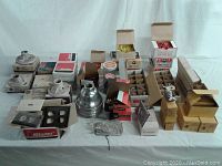 Photo showing assortment of electrical supplies including porcelain lamp holders, wire nuts, switches, receptacles, and lamp shades arranged on a table.