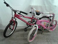Two youth bikes side by side: a hot pink Magna mountain bike with larger knobby tires and a smaller pink Barbie bike with white tires and Barbie decorations.
