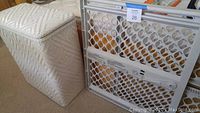 Photo of white woven hamper and plastic adjustable baby gate side by side.