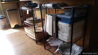 Two black metal wire shelving units each with three adjustable shelves in a room, partially holding containers and plates.