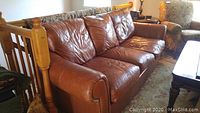 Three-quarter view of brown leather sofa with three seat cushions and rolled arms