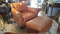 Overall view of brown leather armchair and matching ottoman on area rug.