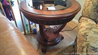 Full view of the round wood side table with a glass insert center and base details.