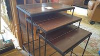 Three solid wood nesting tables shown stacked together. Black metal frames support rectangular wood tops with a rustic finish.
