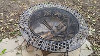Full view of metal fire pit with logs inside, showing diamond weave design and mesh screen