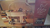 Oval stainless steel chafing dish with glass lid next to its box showing product details