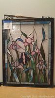Floral stained glass panel with pink and purple flowers, green leaves, and a black frame with blue border. Included hanging bracket visible.