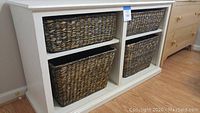 Front view of white wood storage console with four woven basket inserts, showing two rows and two columns of baskets and adjustable shelves inside console.