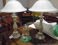 View of the Bulova glass dome clock centered between a pair of celadon lamps with frosted bell-shaped glass shades on a wooden table.