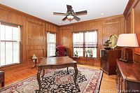 Full view of the area rug laid out in a room with wooden floors and wooden wall paneling, showing its size and color scheme.